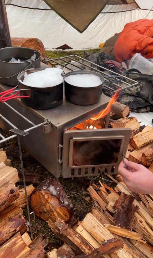 Hot tent wood stove burning firewood with flames out the door