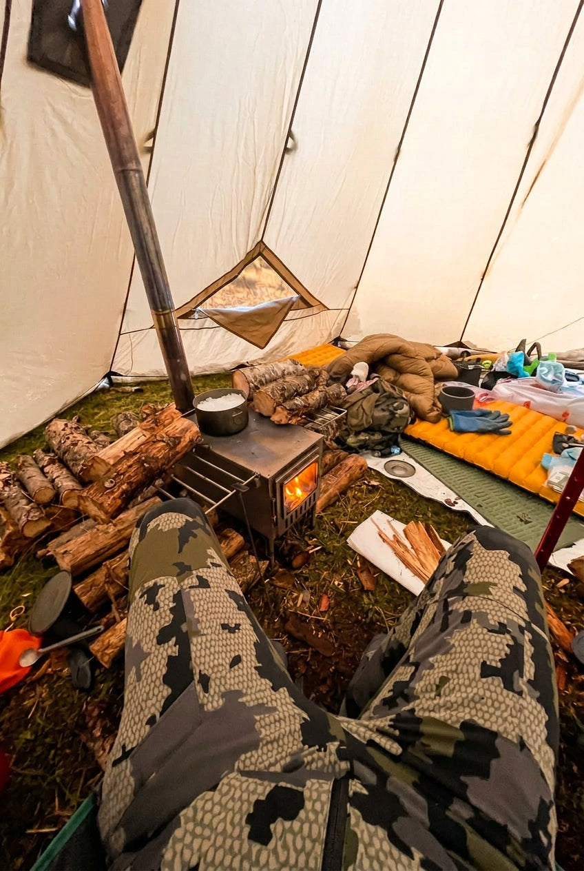 Inside a floorless tent with wood stove and firewood in camp