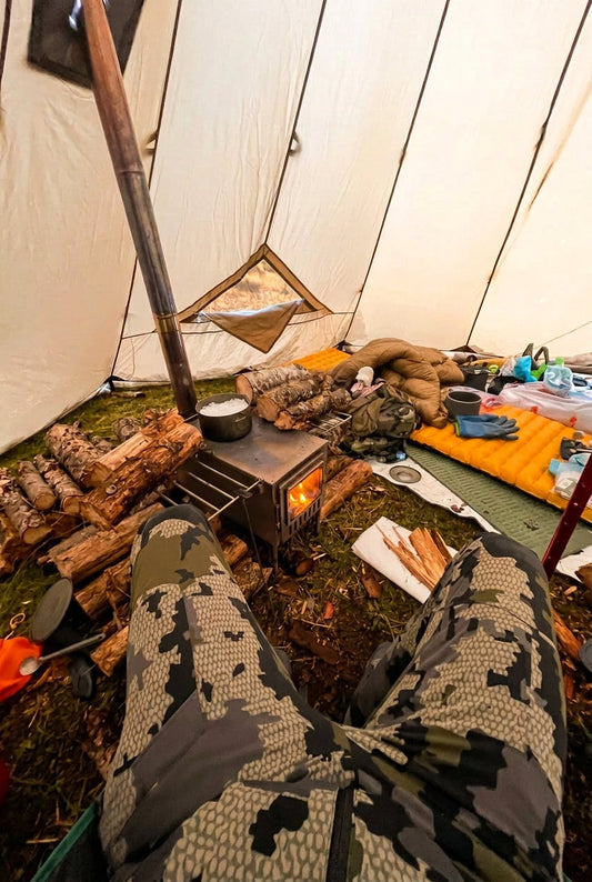 Inside a floorless tent with wood stove and firewood in camp