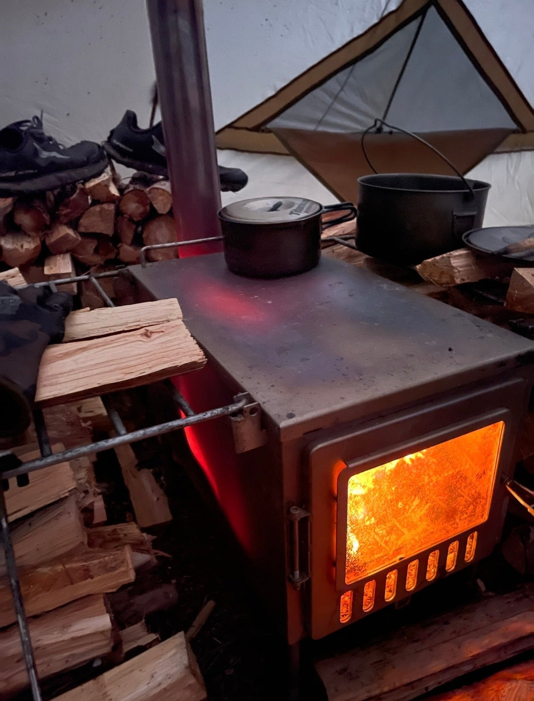 Red hot tent wood stove with firewood pile