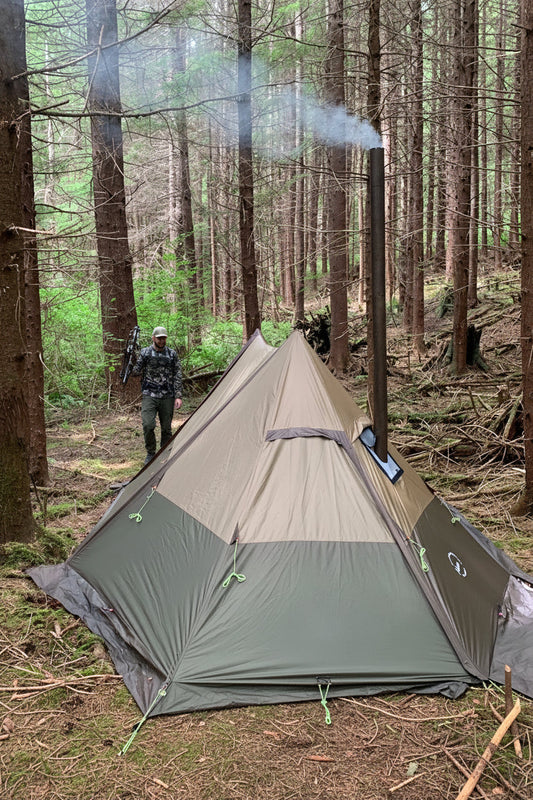 Hot tent with wood stove jack inside forest campsite