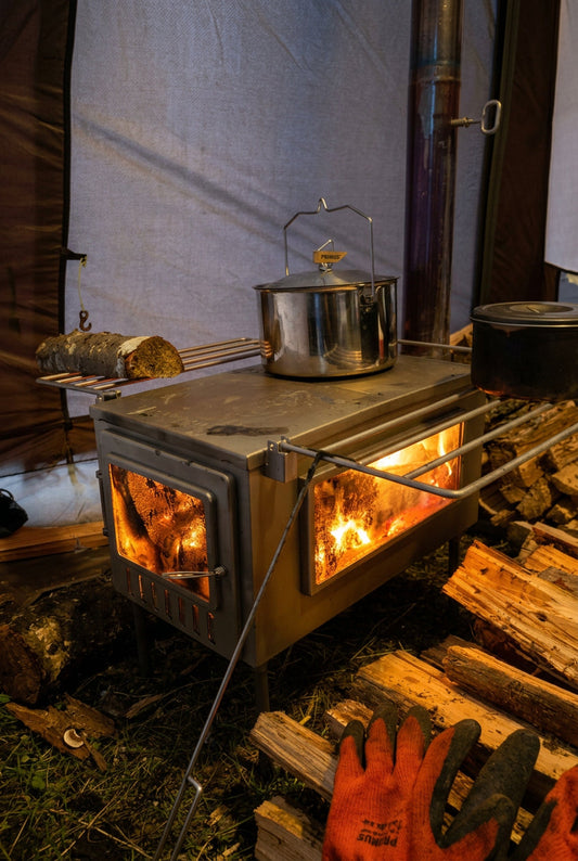 Tent wood stove inside campsite with firewood and pot on stovetop