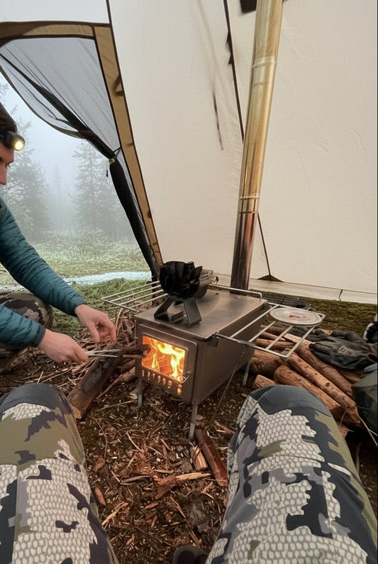 Tent wood stove inside shelter with firewood in foggy mountain campsite