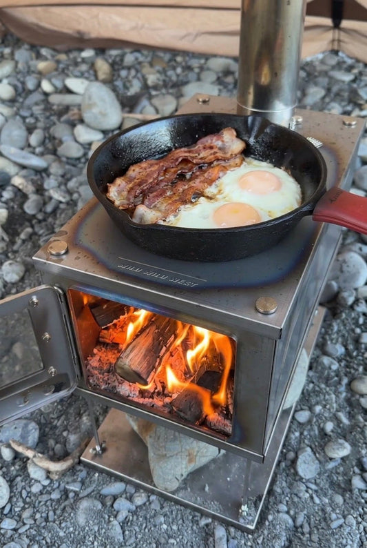 Titanium tent stove burning firewood and cooking breakfast on the stovetop in a cast iron pan