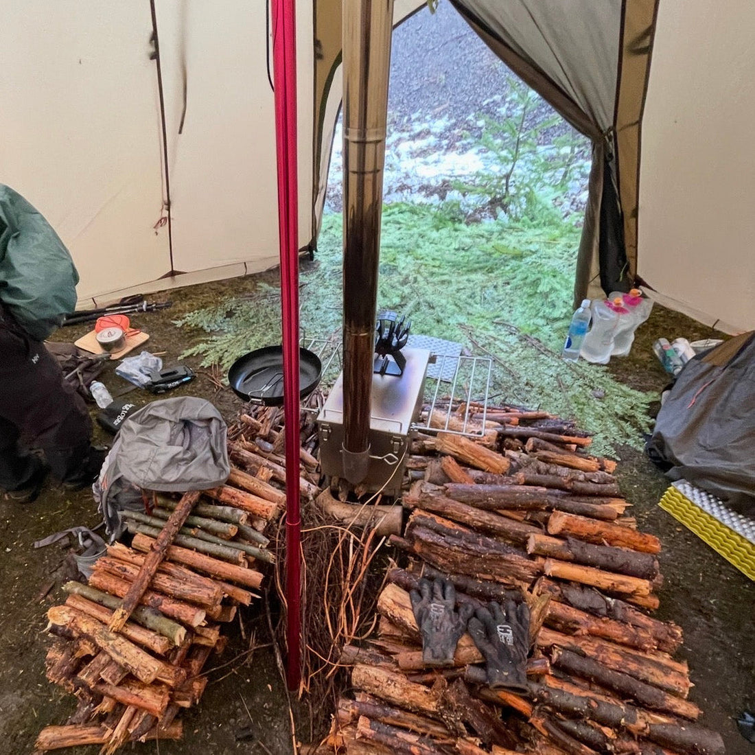 Wet firewood stacked next to tent wood stove inside shelter floor while camping