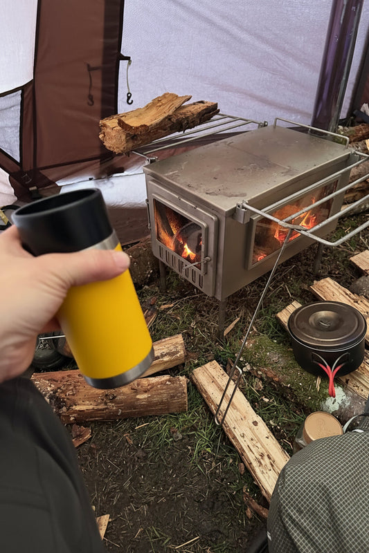 Wood stove inside hot tent with firewood and morning coffee