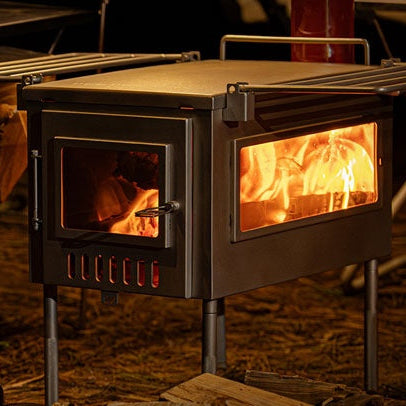X-stove XL Hot Tent Stove with a warm fire inside, surrounded by camping furniture in a dimly lit campsite.